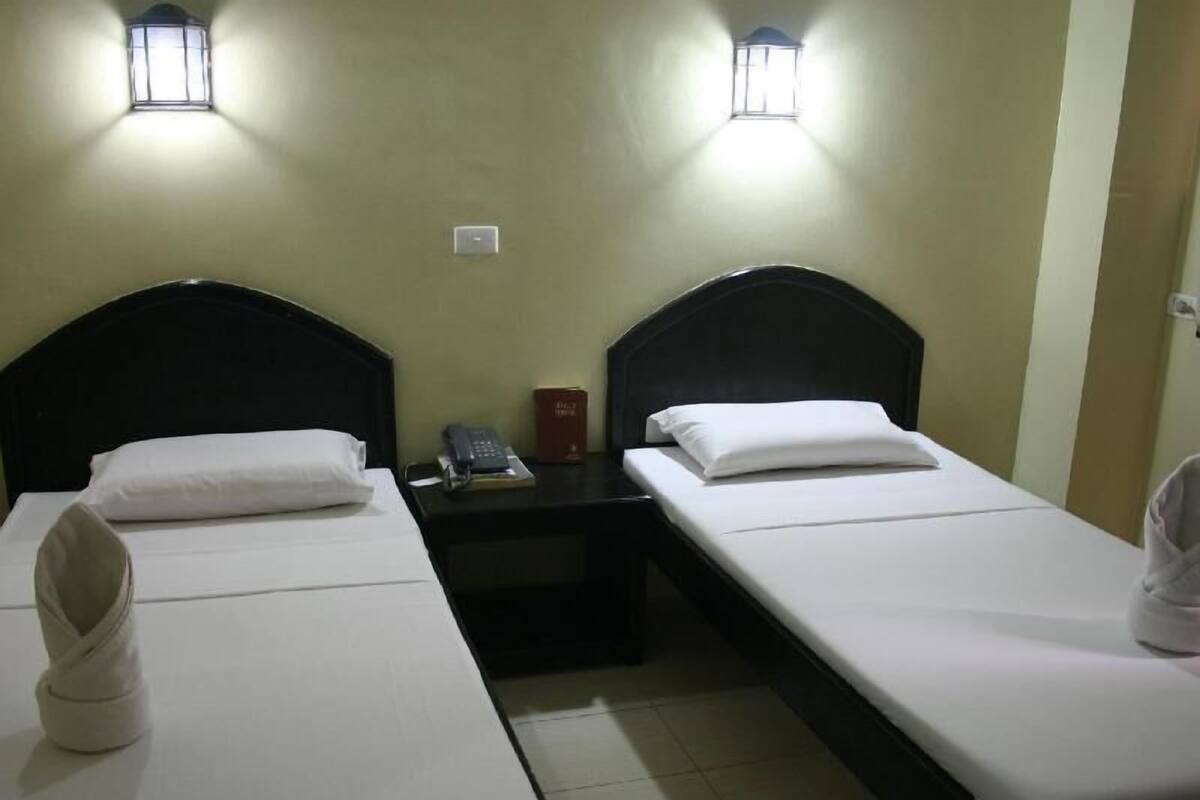 Ein Hotelzimmer mit zwei Einzelbetten, einem Nachttisch mit Telefon und Buch sowie zwei Wandlampen.