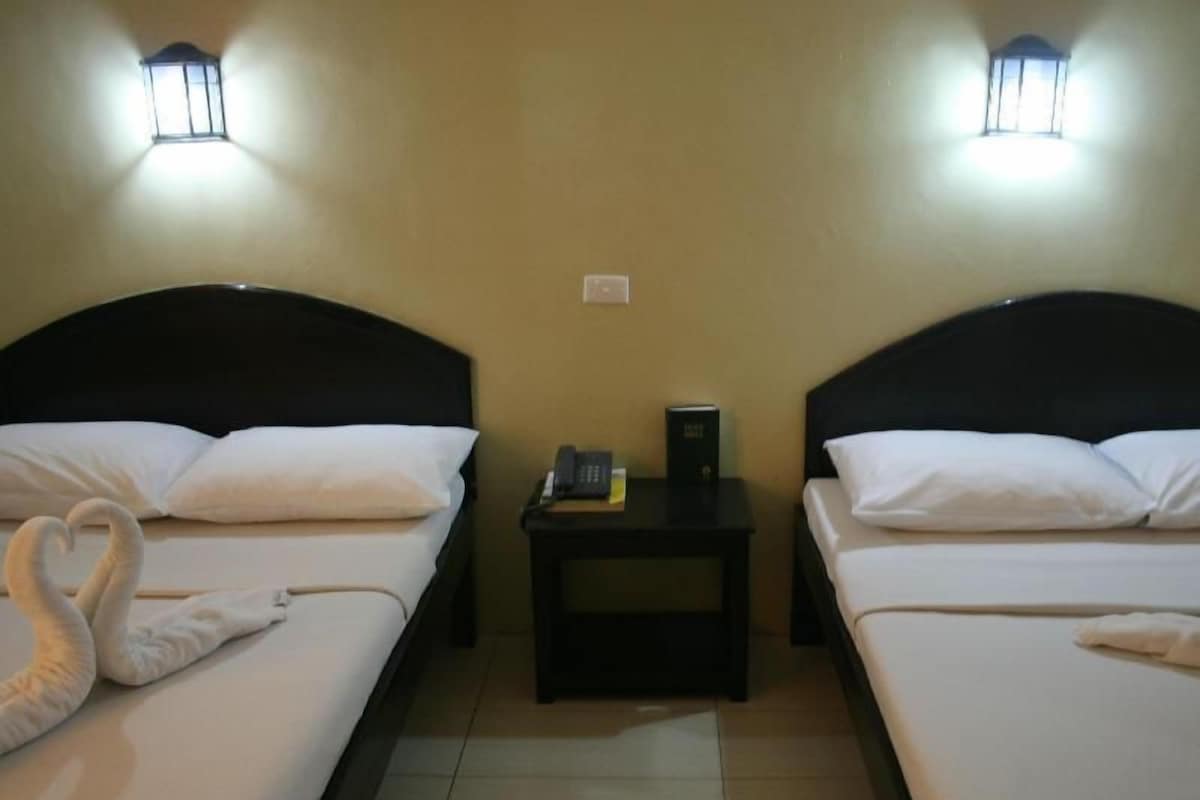 A hotel room with two beds, each with white bedding and a dark headboard. There are two bedside tables with a lamp and a book on one.