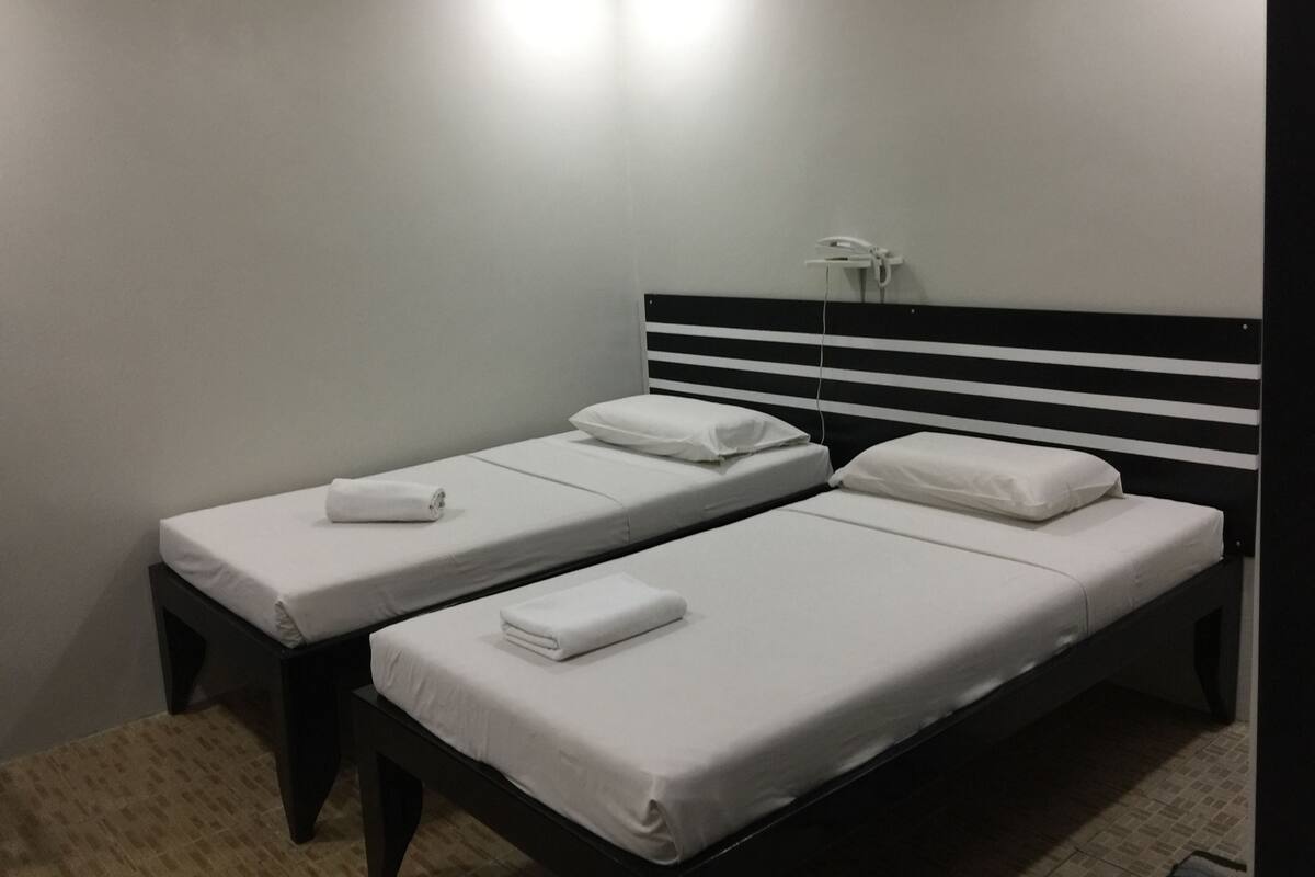 Ein Zimmer mit zwei Einzelbetten, jedes mit einer weißen Matratze und einem Kissen, und einem schwarzen Kopfteil.