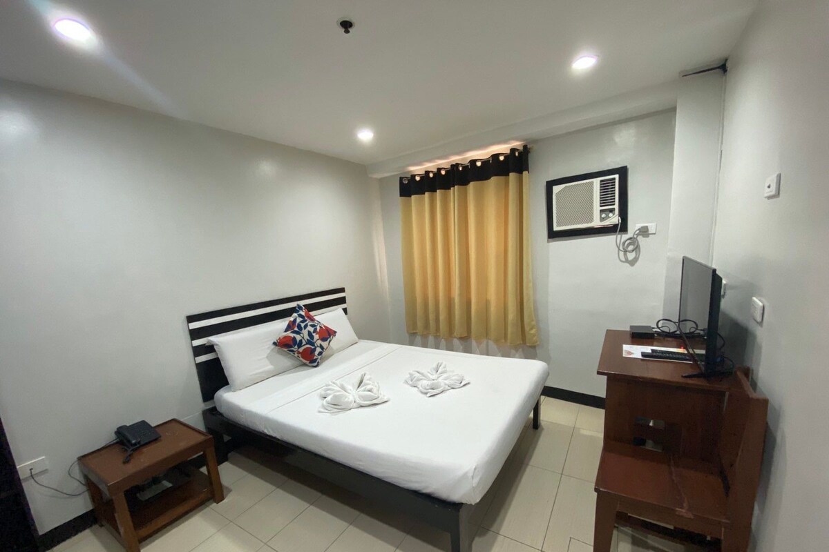 A hotel room with a bed, a desk, a chair, a telephone, and a television.