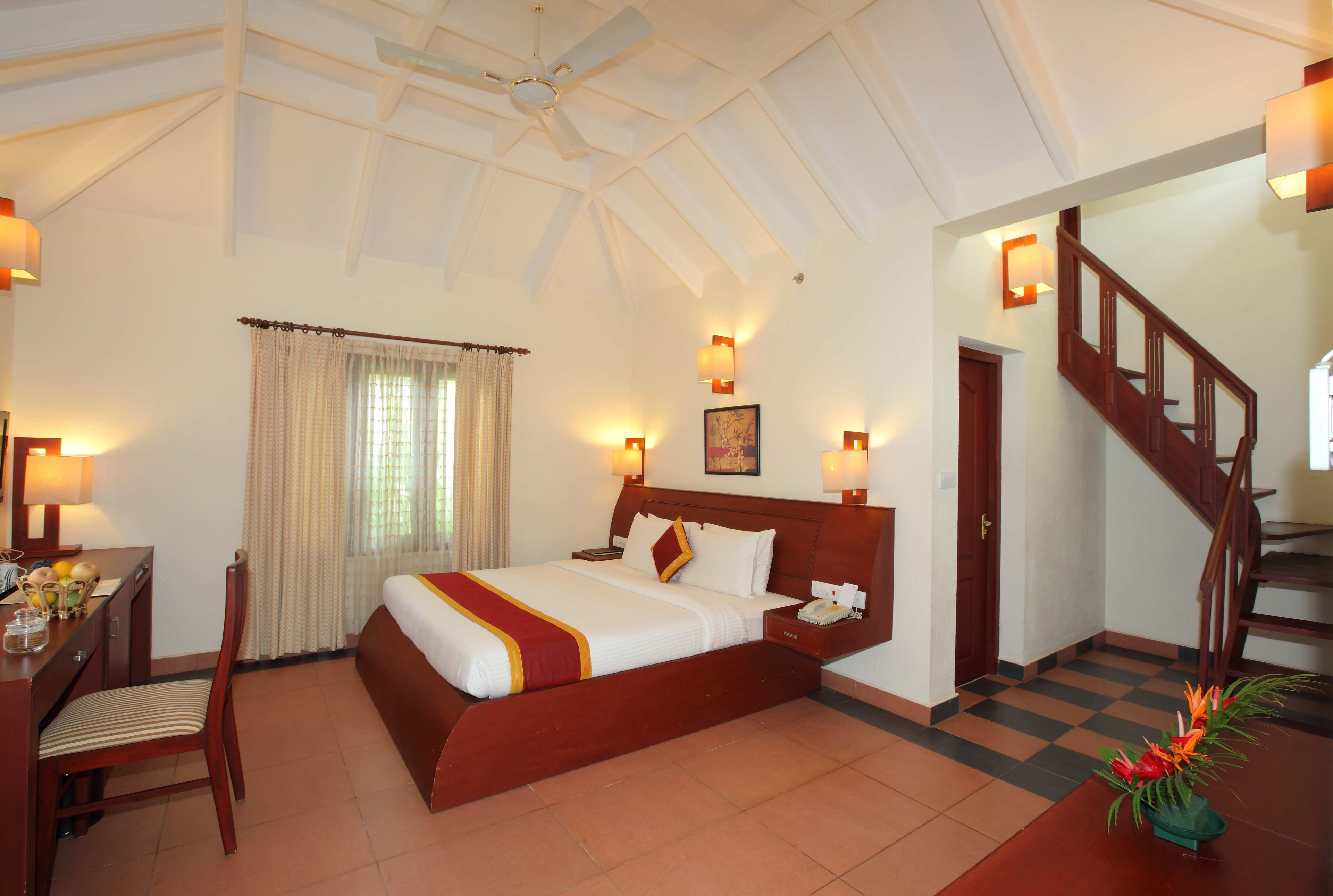 A hotel room with a large bed, a desk with a chair, a staircase, and a ceiling fan.