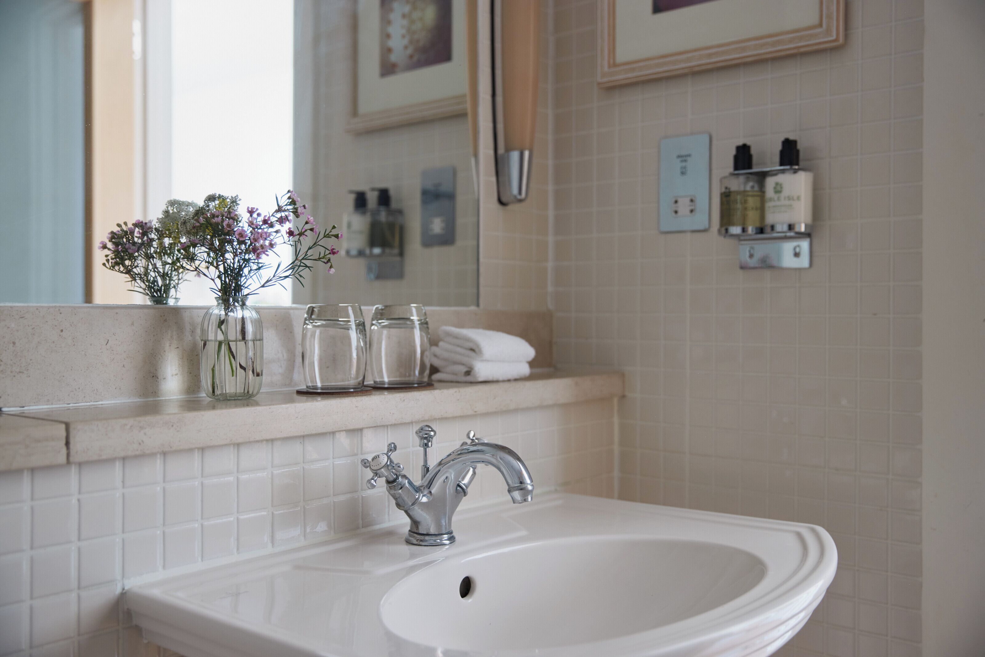 A bathroom with a white sink, a mirror, and a vase with flowers on the countertop.