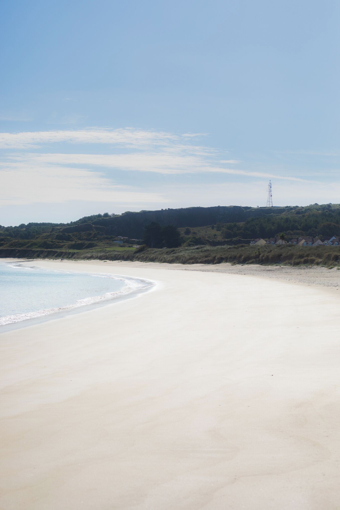 Une plage avec un ciel dégagé, un rivage sablonneux et, au loin, une colline surmontée d’une tour.