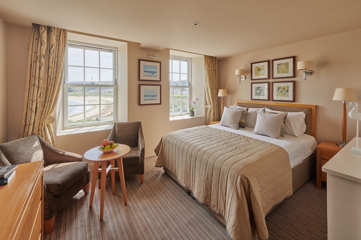 A hotel room with a large bed, a desk, a chair, a small table with fruit, and a view of the landscape through the window.