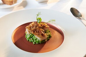 Une assiette de nourriture comprenant une noix de Saint-Jacques et des légumes verts, le tout présenté sur une assiette de couleur cuivrée.