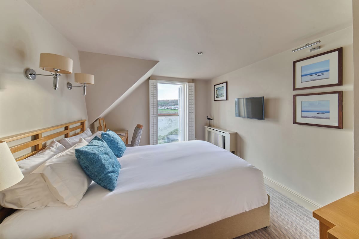 A hotel room with a bed, a desk, a chair, a TV, and a window with a view of the beach.