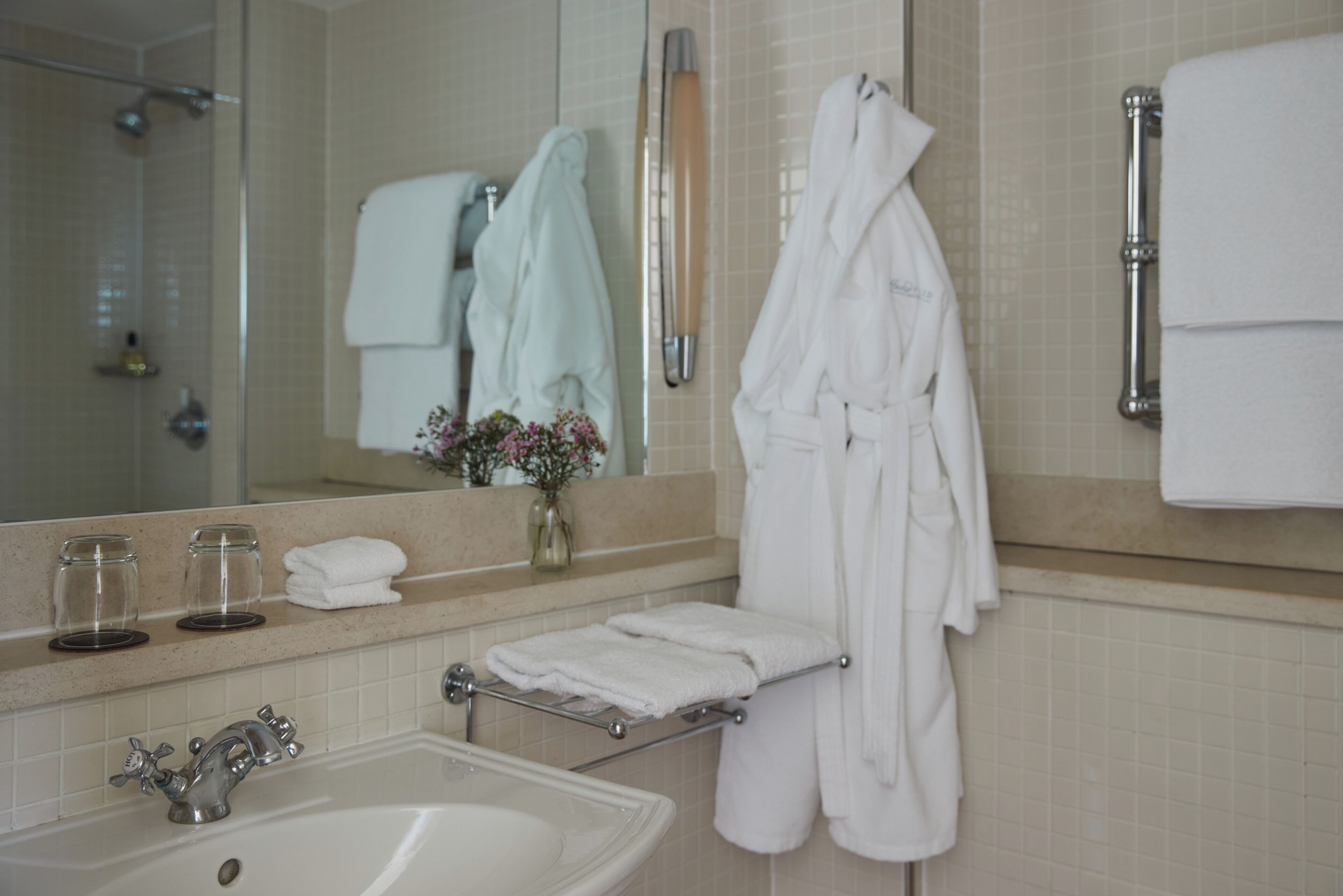 Un baño con lavamanos, espejo, toallero y zona de ducha.