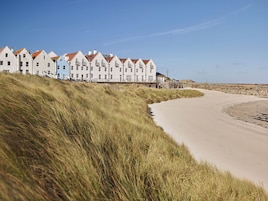 Una hilera de casas costeras con una playa de arena y dunas cubiertas de hierba.