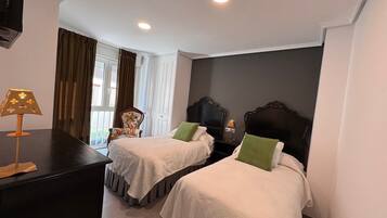 A hotel room with two beds, a desk, a chair, and a window with curtains.