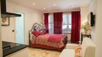 A bedroom with a bed, a sofa, a small table, and a window with red curtains.