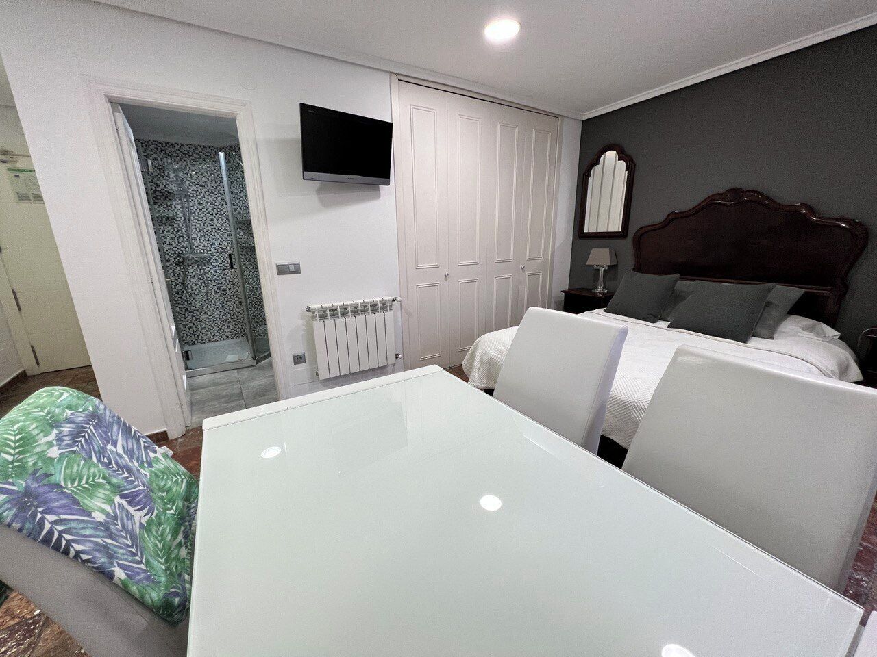 Un dormitorio con cama, televisor, armario blanco y ducha.