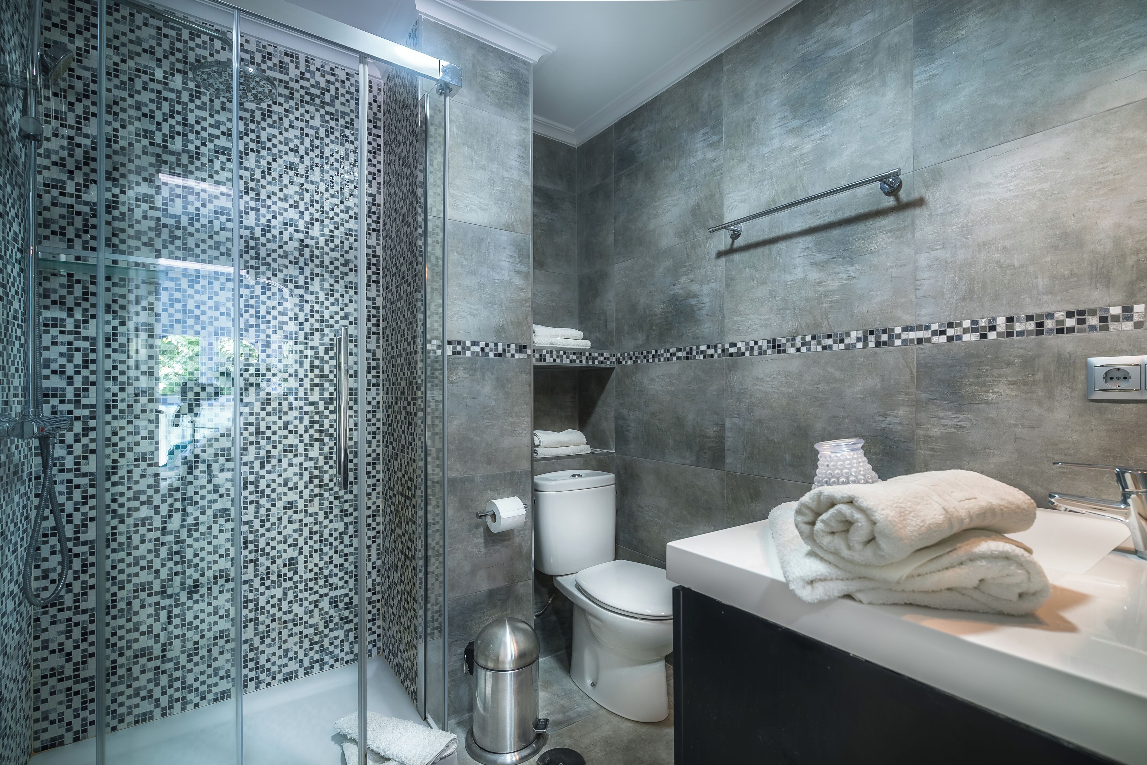 A modern bathroom with a glass-enclosed shower, a toilet, and a vanity with towels.