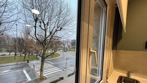A view from a window of a room with a sink and a view of a road with a crosswalk and trees. - Apartamentos Las Brisas (Santander)