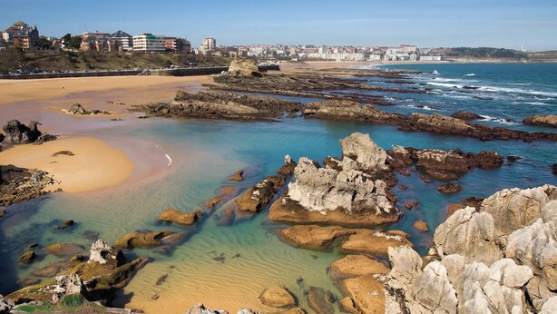 A coastal landscape with clear waters, rocky formations, and a sandy beach. - Apartamentos Las Brisas (Santander)