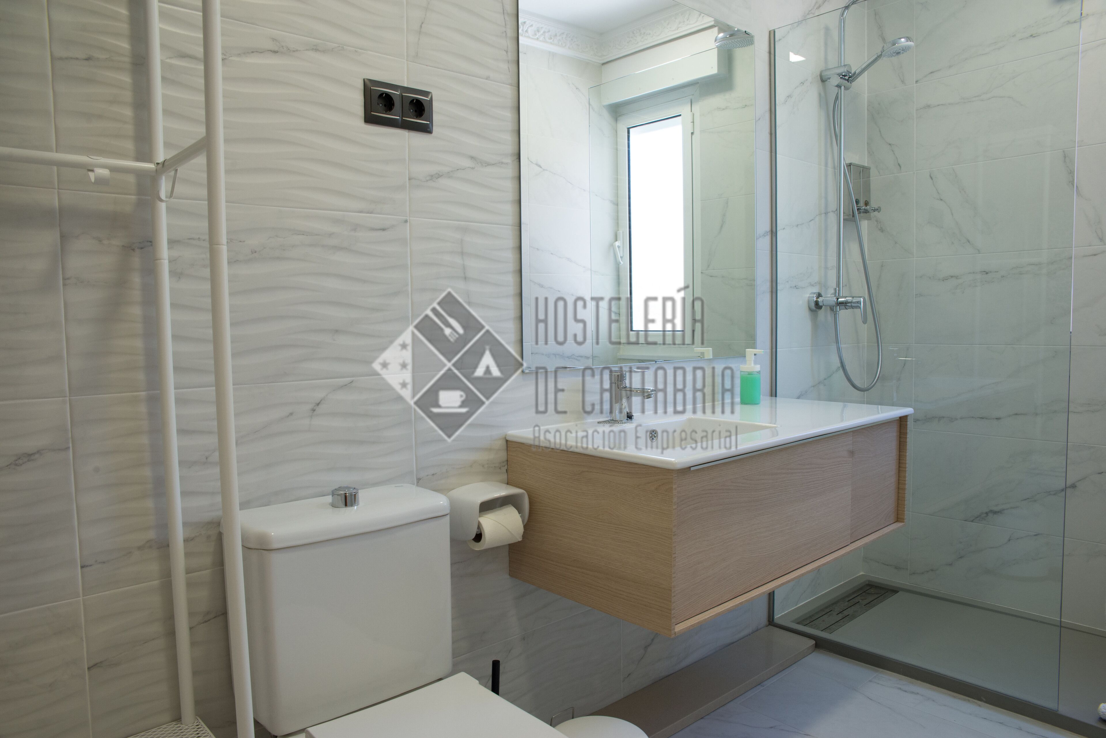 A modern bathroom with a marble wall, a wooden vanity, a glass shower enclosure, and a toilet.