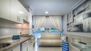 A compact kitchen with white cabinets, a washing machine, and a dining area with a glass table and chairs. - Apartamentos Las Brisas (Santander)