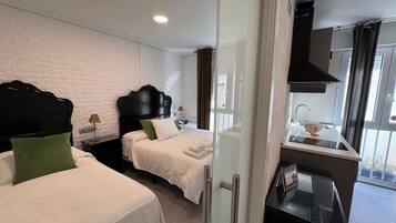 Habitació d'hotel amb dos llits, una cuineta i una finestra gran.