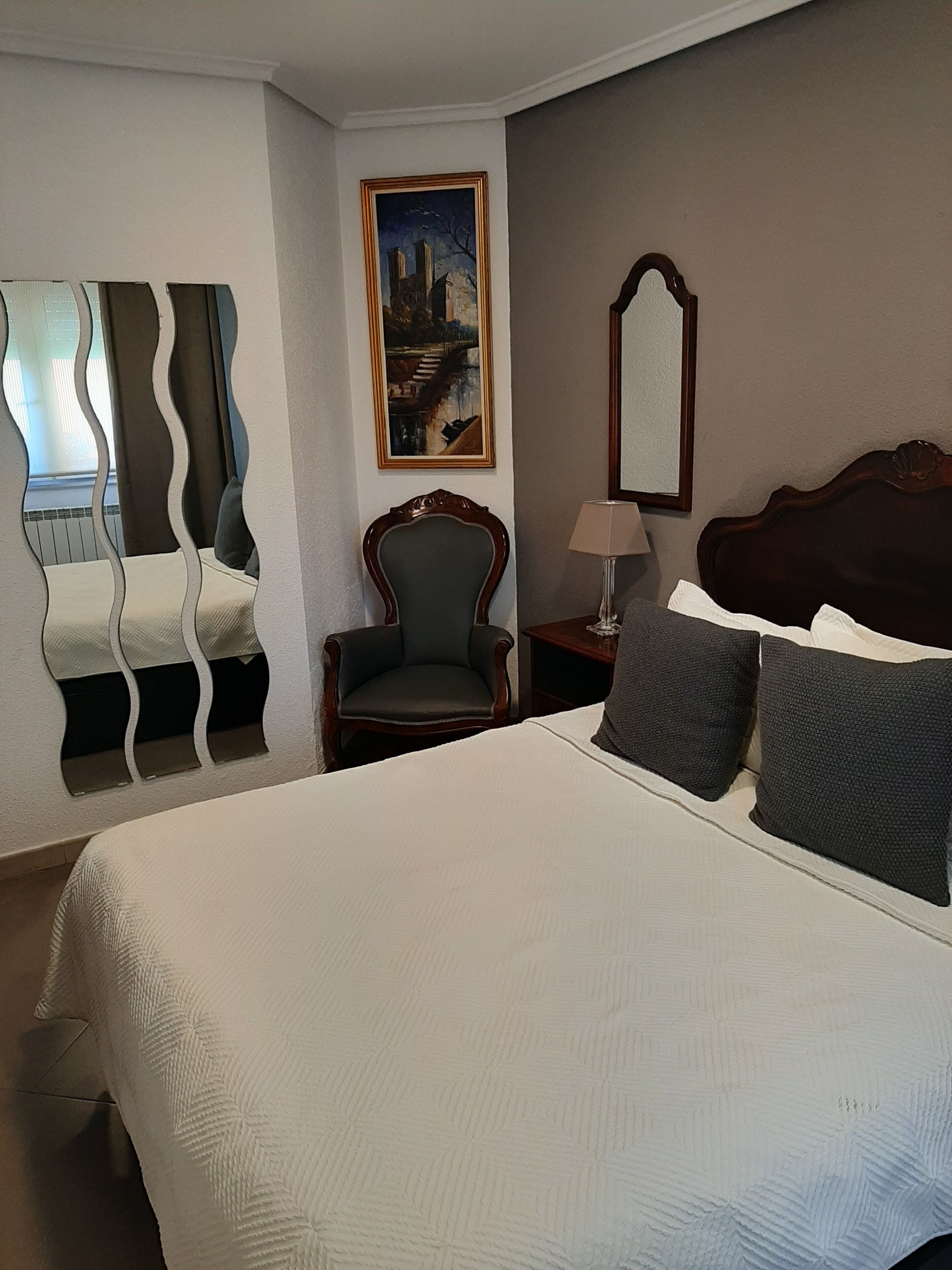 A hotel room with a large bed, a chair, a painting on the wall, and a mirror.