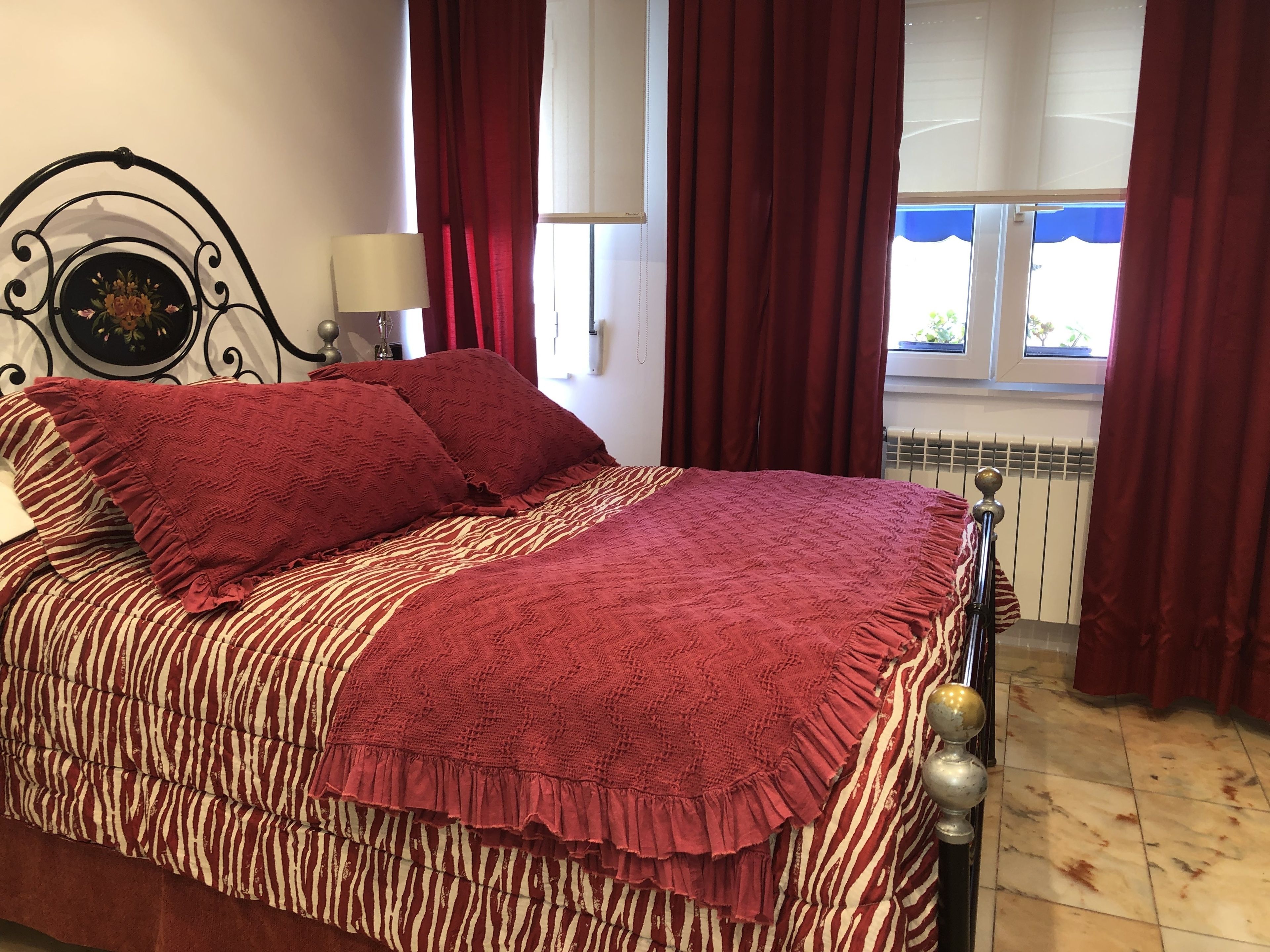 Een net opgemaakt bed met een deken met strepen en een zebraprint, rode kussens en een bijpassend rode plaid.