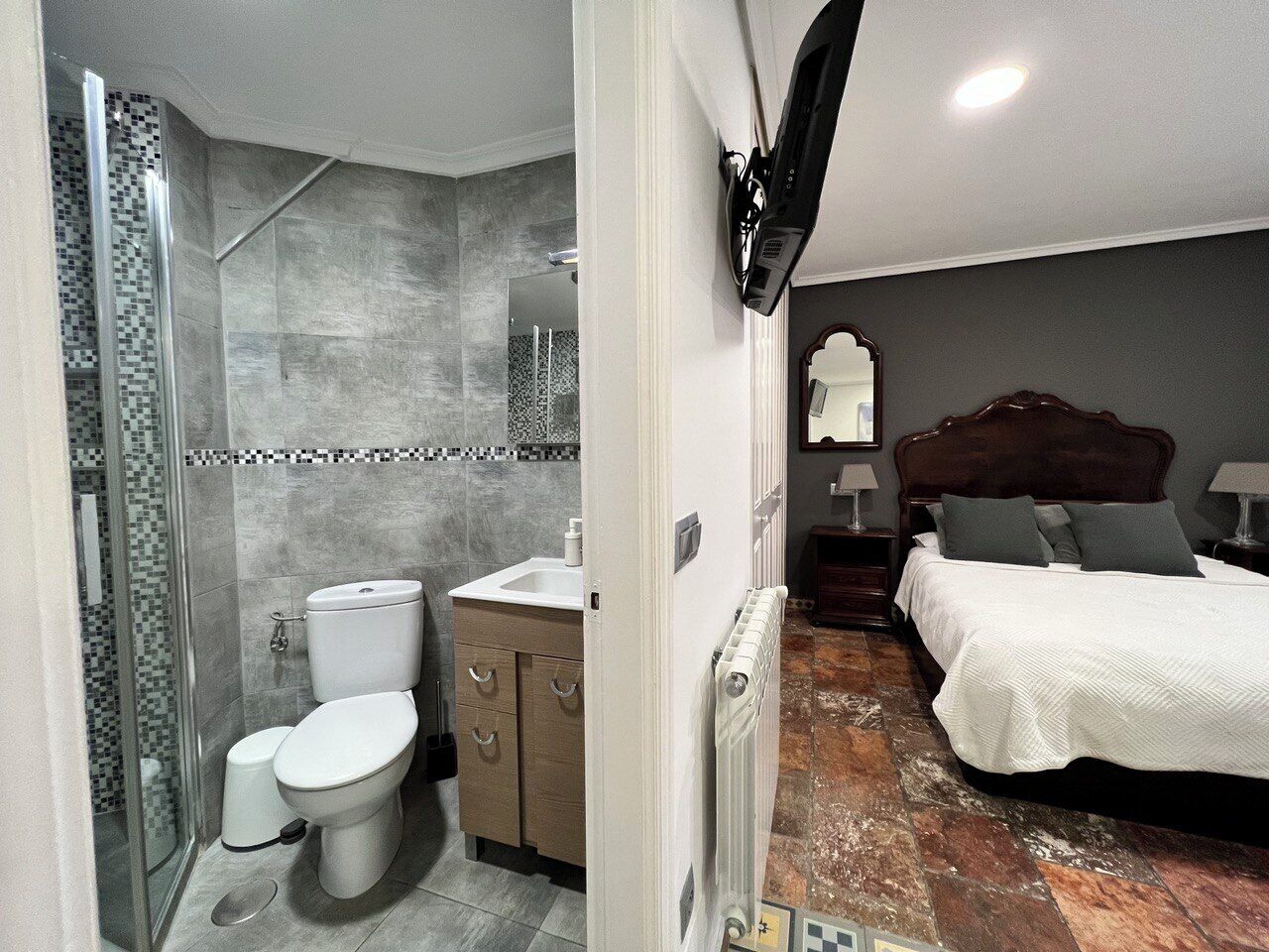 A bathroom with a shower, toilet, and sink, and a bedroom with a bed and nightstand.