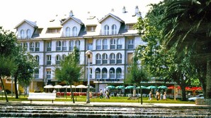 A large hotel with multiple stories, a fountain in the foreground, and outdoor seating areas with umbrellas. - Apartamentos Las Brisas (Santander)