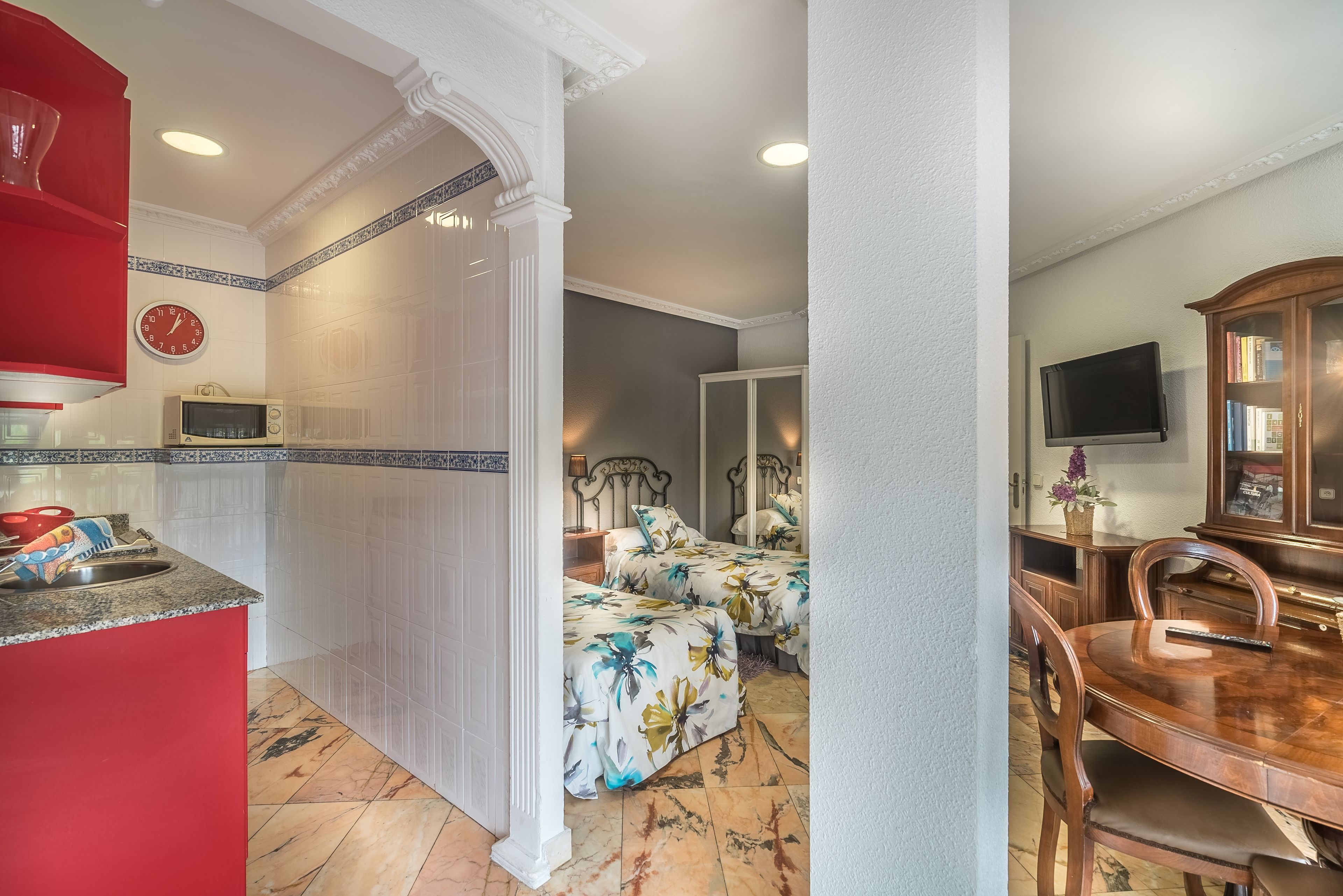 A compact living space with a kitchen area, a dining table, and a bedroom with two beds.