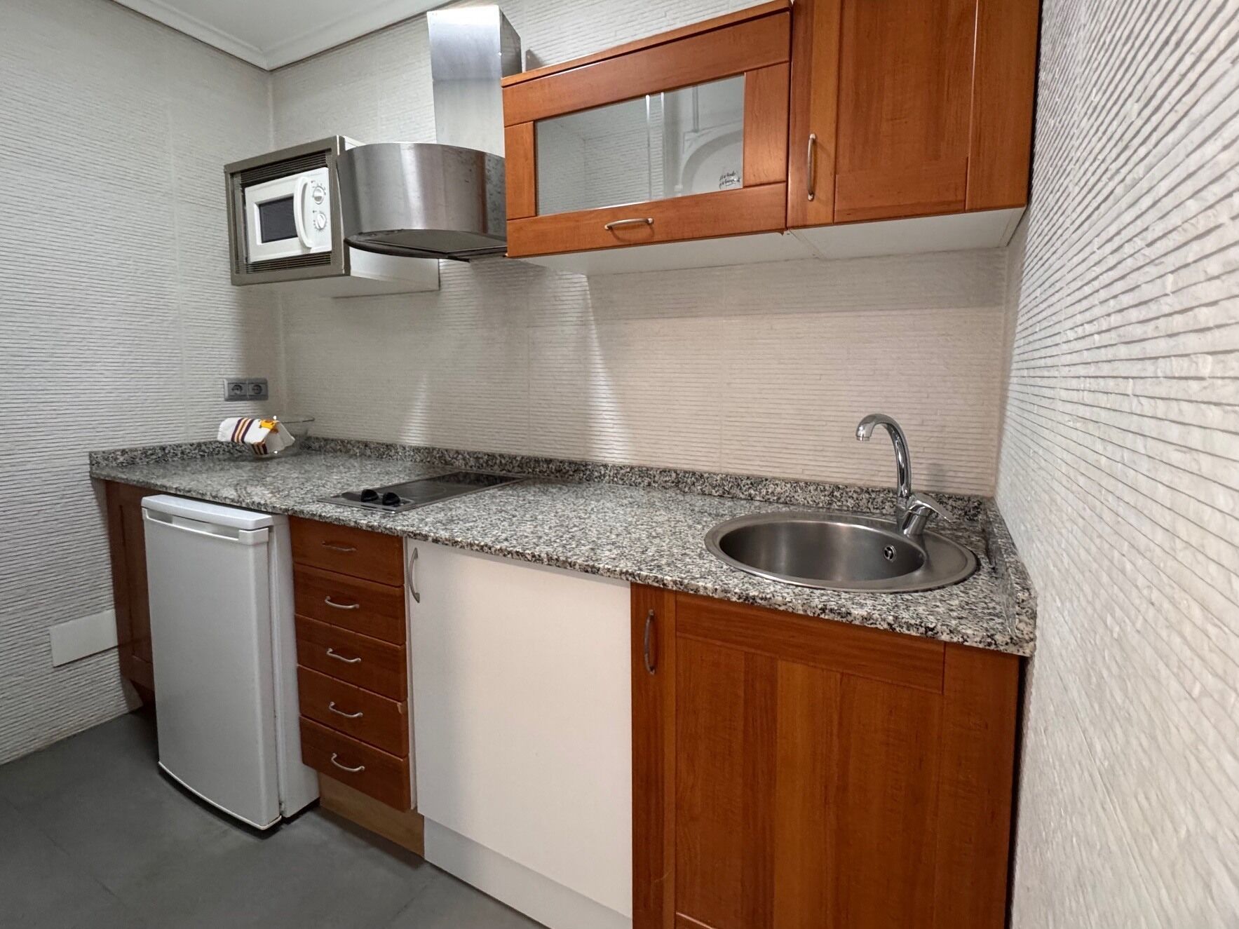 A compact kitchen with a built-in microwave, stainless steel sink, and a dishwasher.