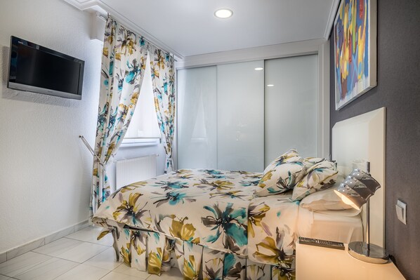 A bedroom with a bed, curtains, a TV, a bedside lamp, and a painting on the wall. - Apartamentos Las Brisas (Santander)