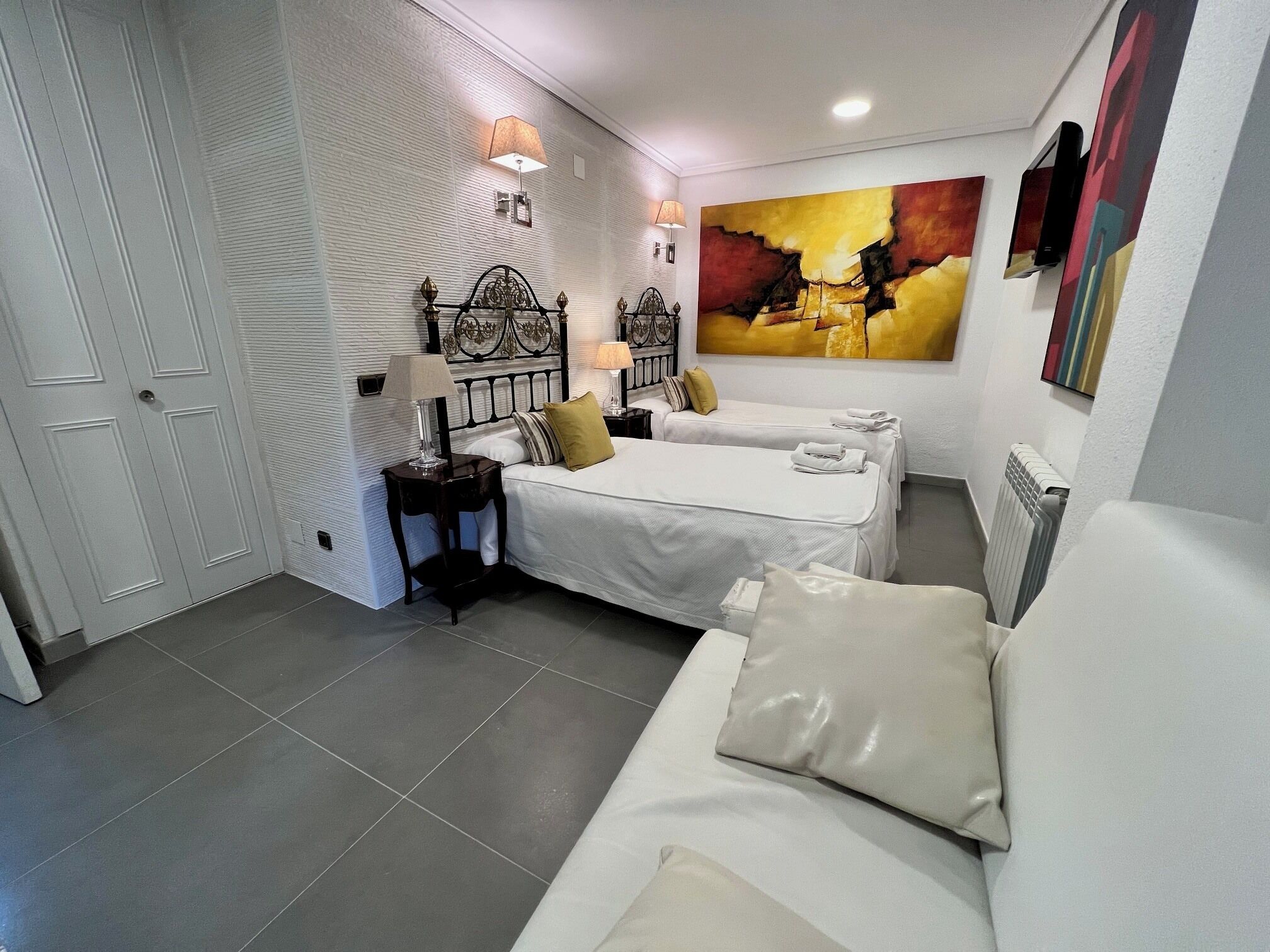 Un dormitorio con una cama, mesitas de noche, una lámpara, un radiador y un cuadro en la pared.