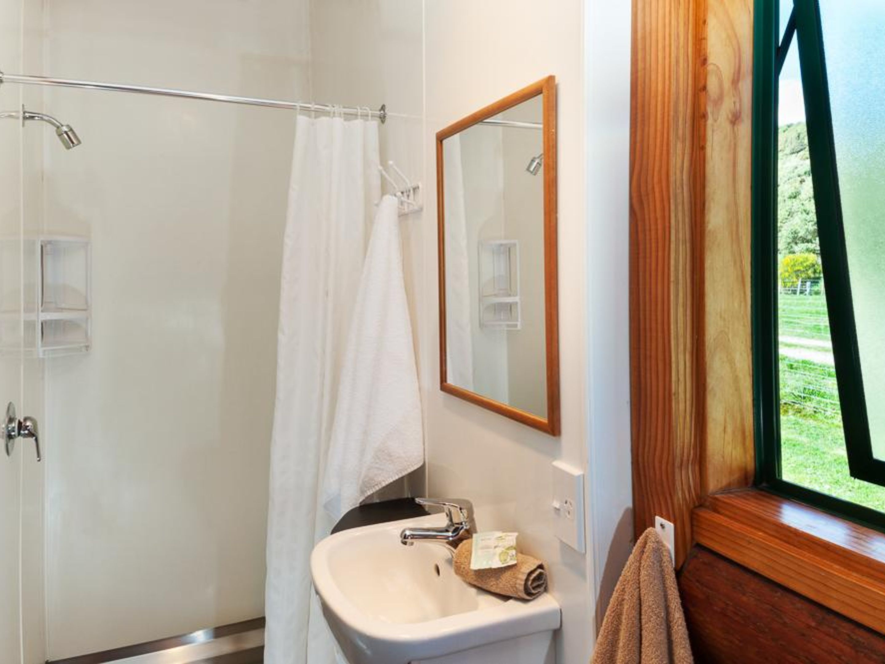 A bathroom with a shower, a sink, a mirror, and a window.