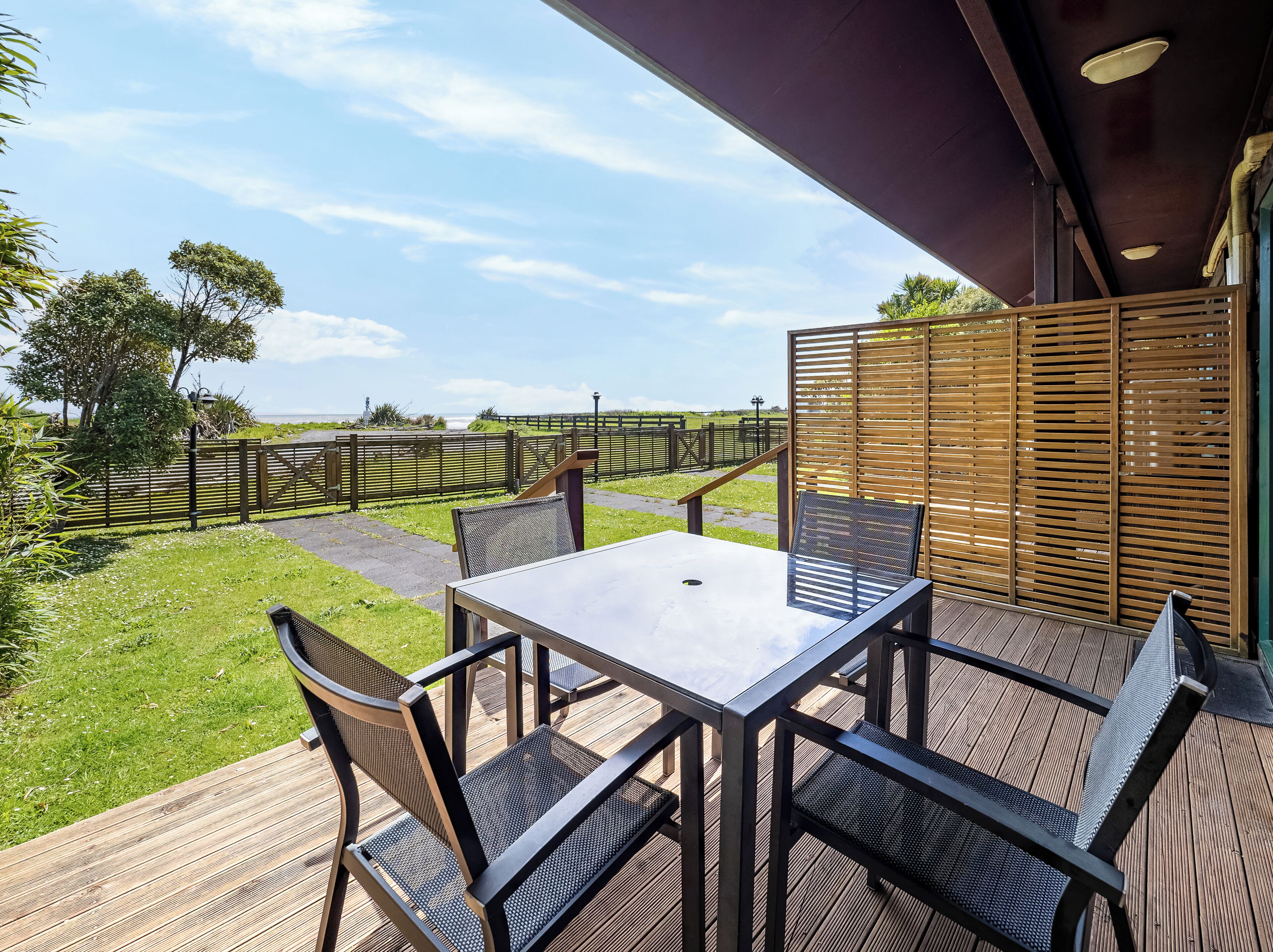 Un patio al aire libre con una mesa y sillas, una valla de madera y vistas al mar.