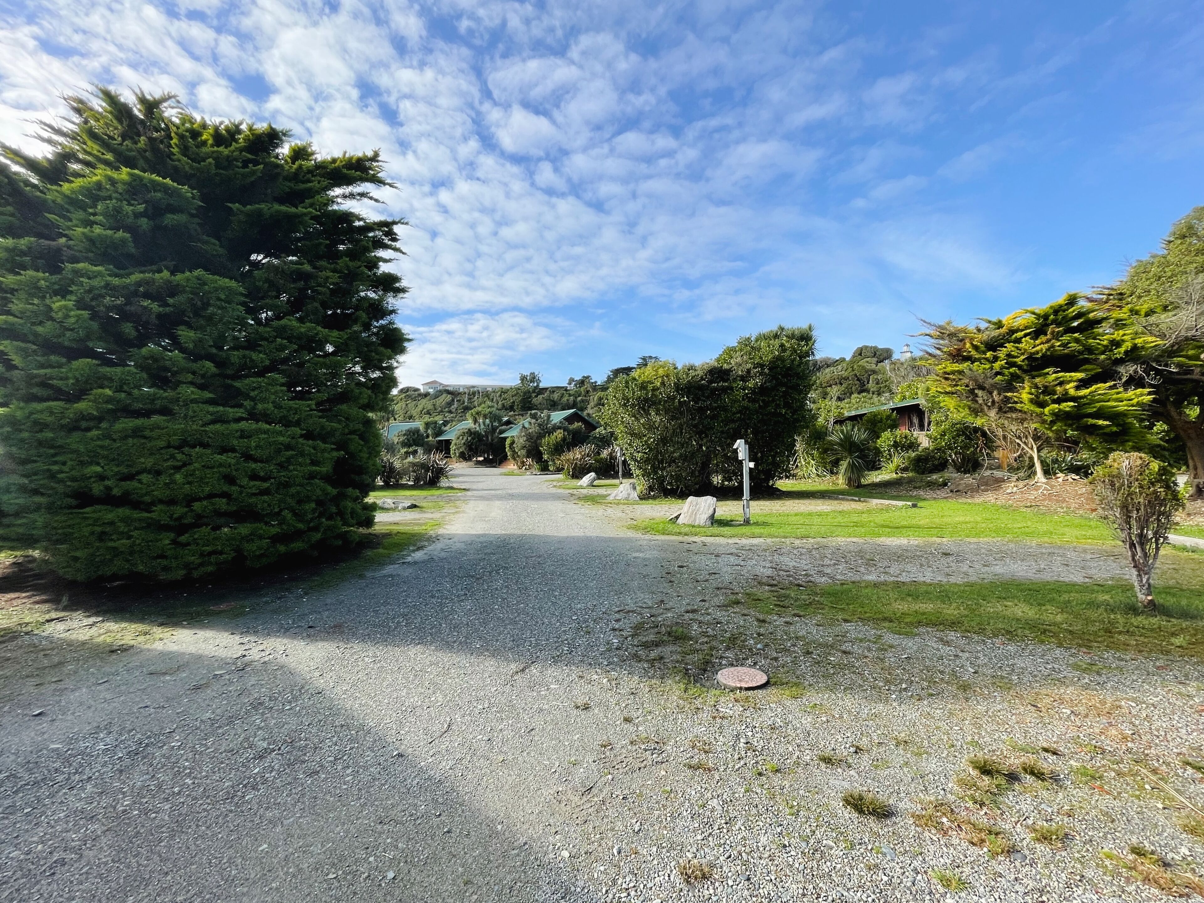 A gravel path leading through a landscaped area with various trees and shrubs, a signpost, and a building in the background.