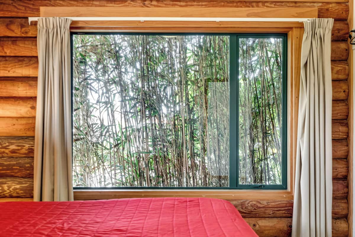 A room with a large window, wooden walls, and a red bedspread.