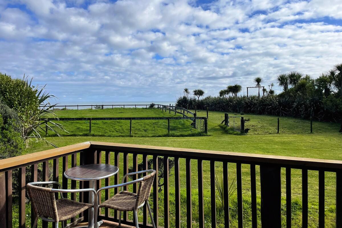 A patio with a table and chairs, overlooking a grassy area with a fence and palm trees.