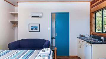 Una habitación pequeña con una cama, una puerta azul, una kitchenette y un cuadro en la pared.