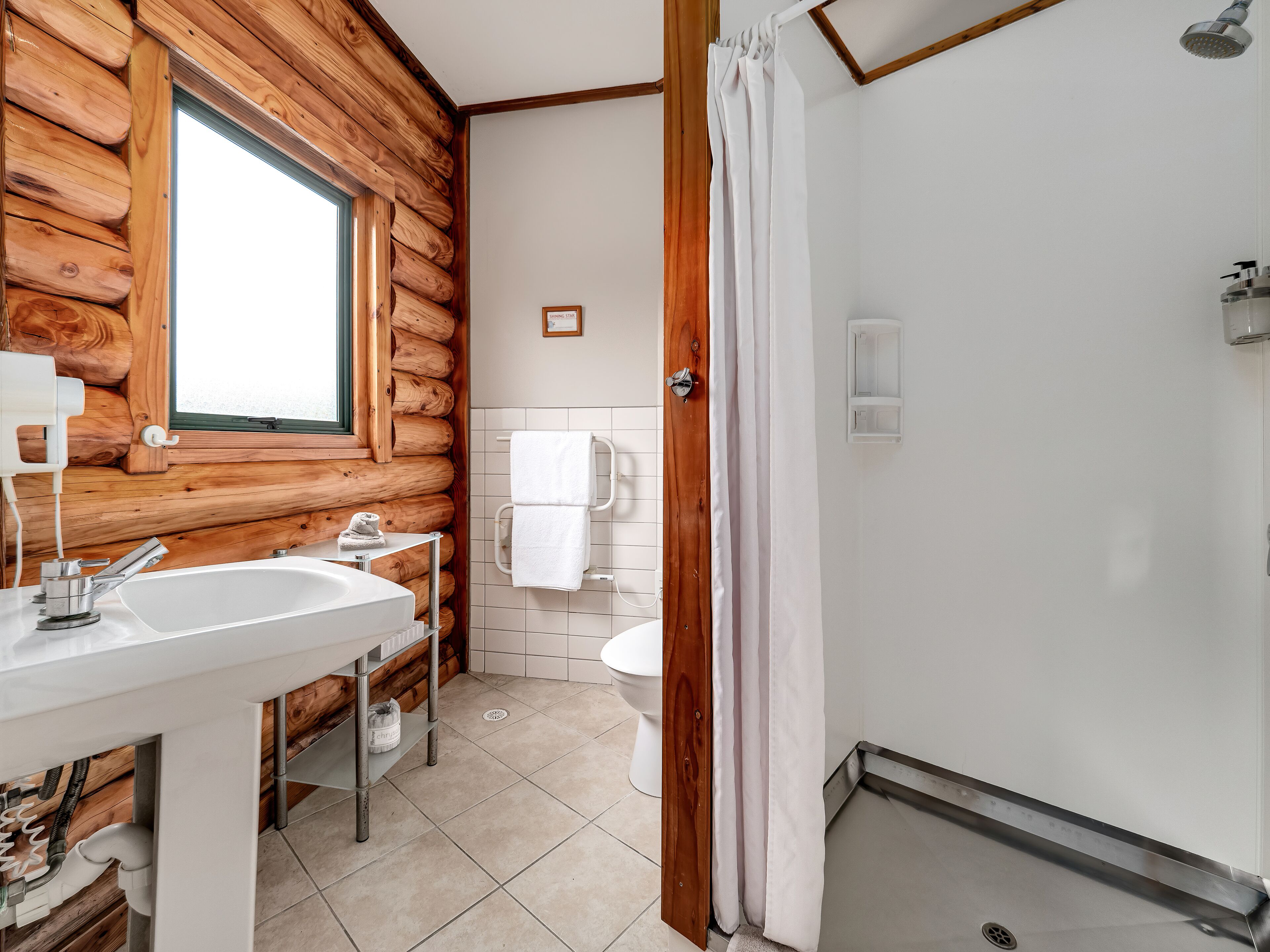 A bathroom with a wooden log wall, a sink, a toilet, and a shower area.