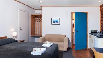 A hotel room with a large bed, a chair, a desk with a sink, and a wardrobe.