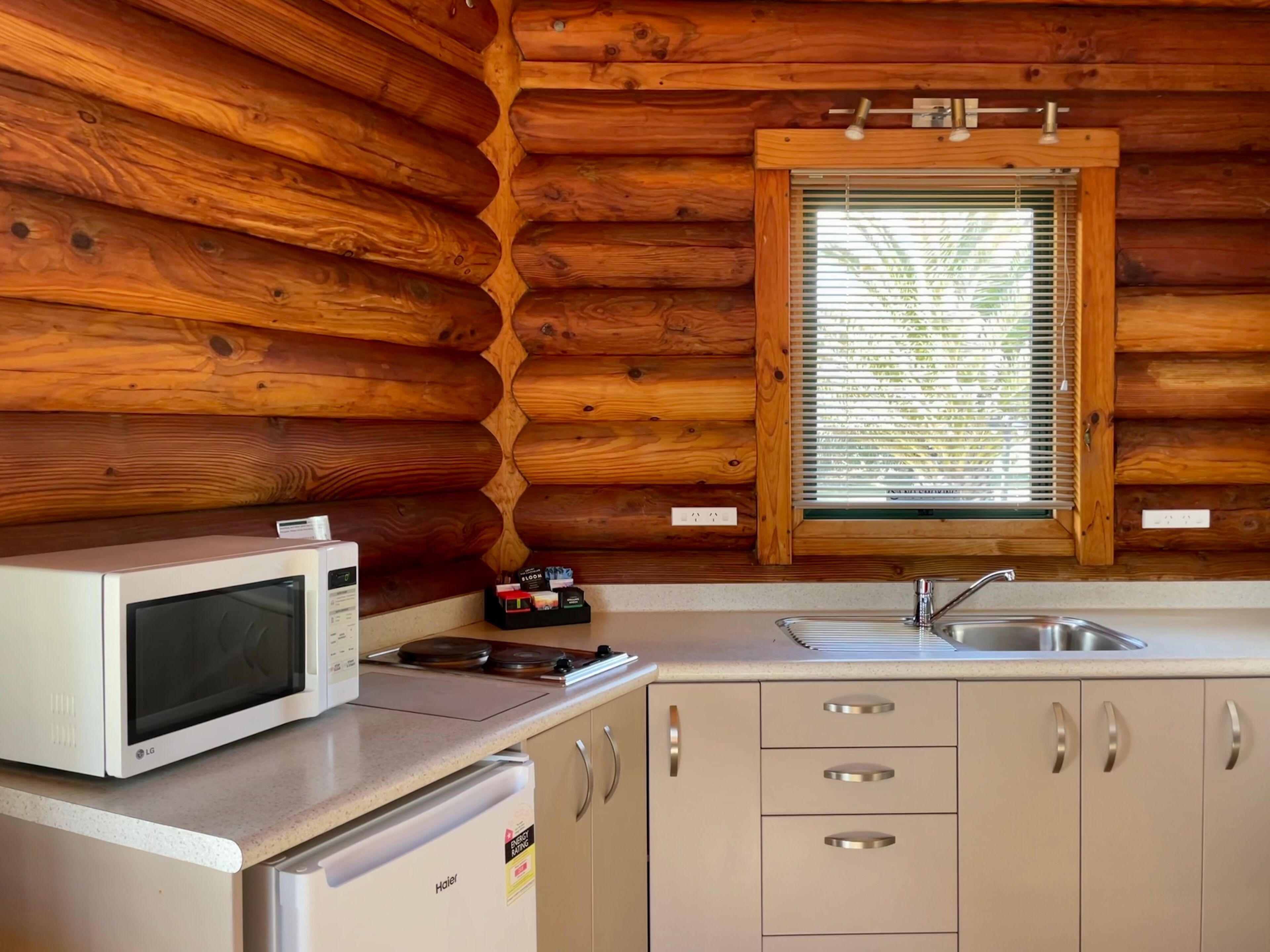 A compact kitchen with wooden log walls, a microwave, a small stove, a sink, and a refrigerator.