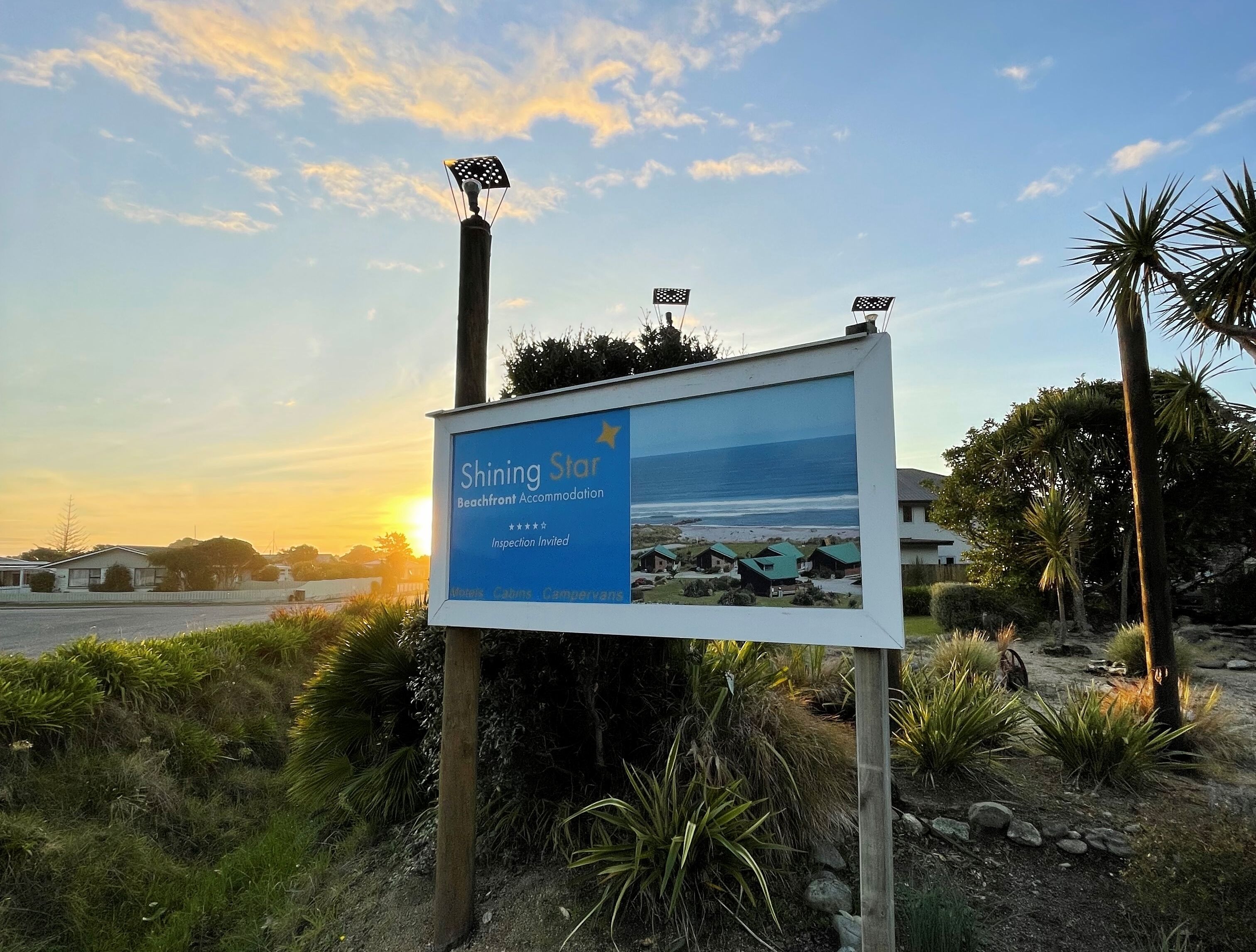 A sign for 'Shining Star Beachfront Accommodation' with a view of the beach and houses in the background.
