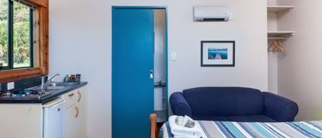 Quarto compacto com cozinha compacta, cama com roupa de cama listrada, porta azul e quadro na parede.