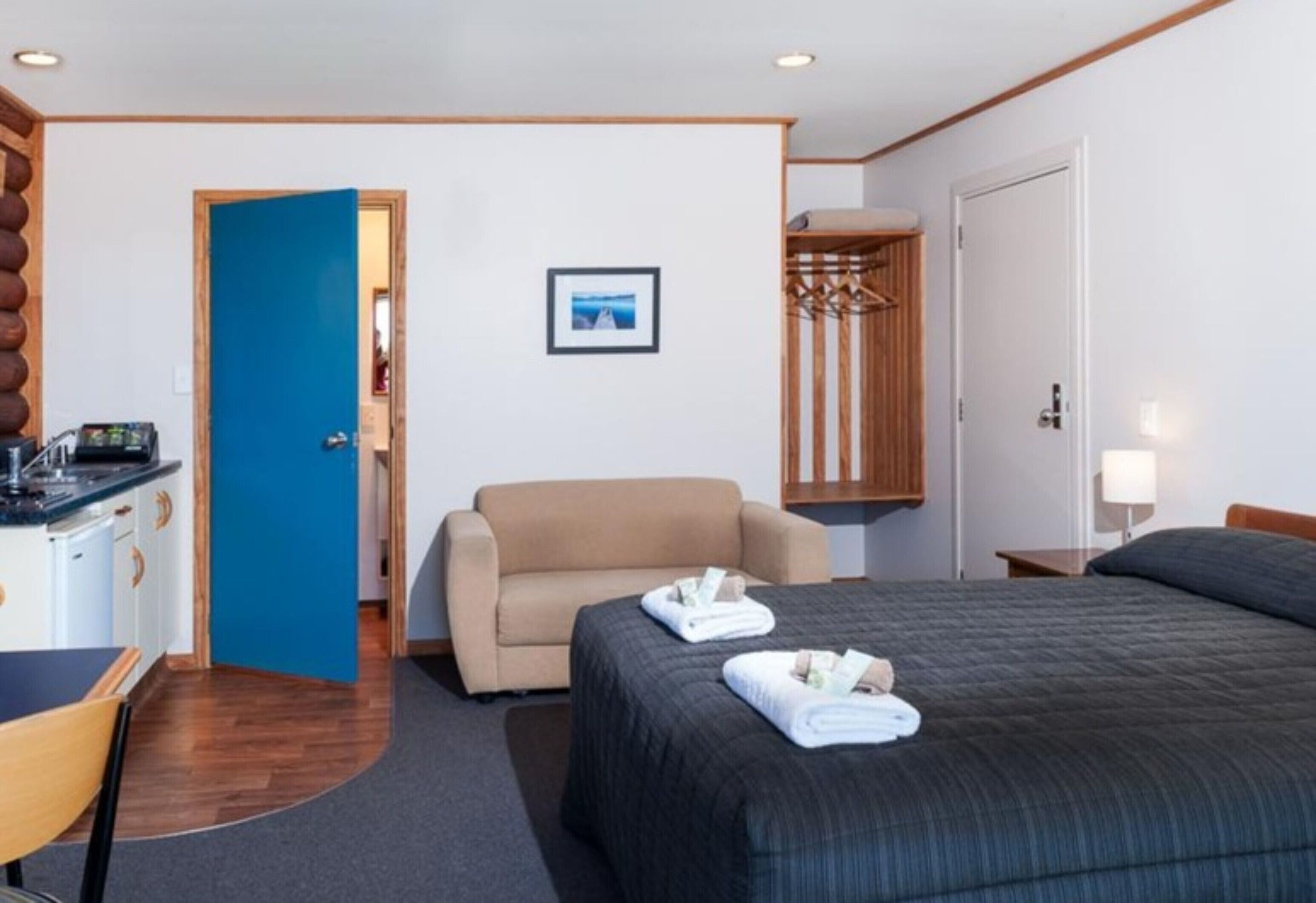 Quarto de hotel com cama, sofá, escrivaninha com computador e porta que dá para outro quarto.
