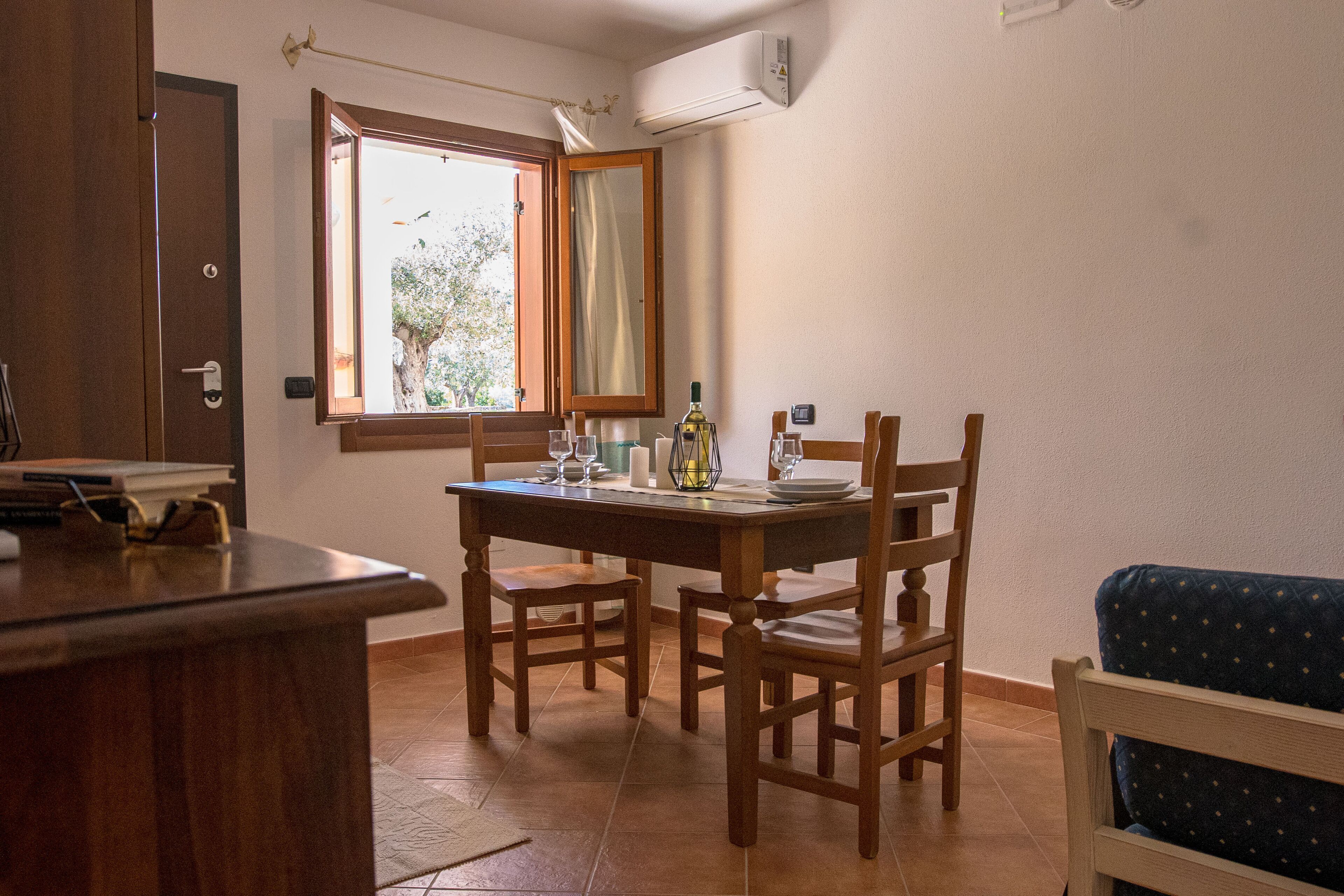 Un comedor con una mesa y sillas de madera, una ventana con cortina abierta y un sofá azul.