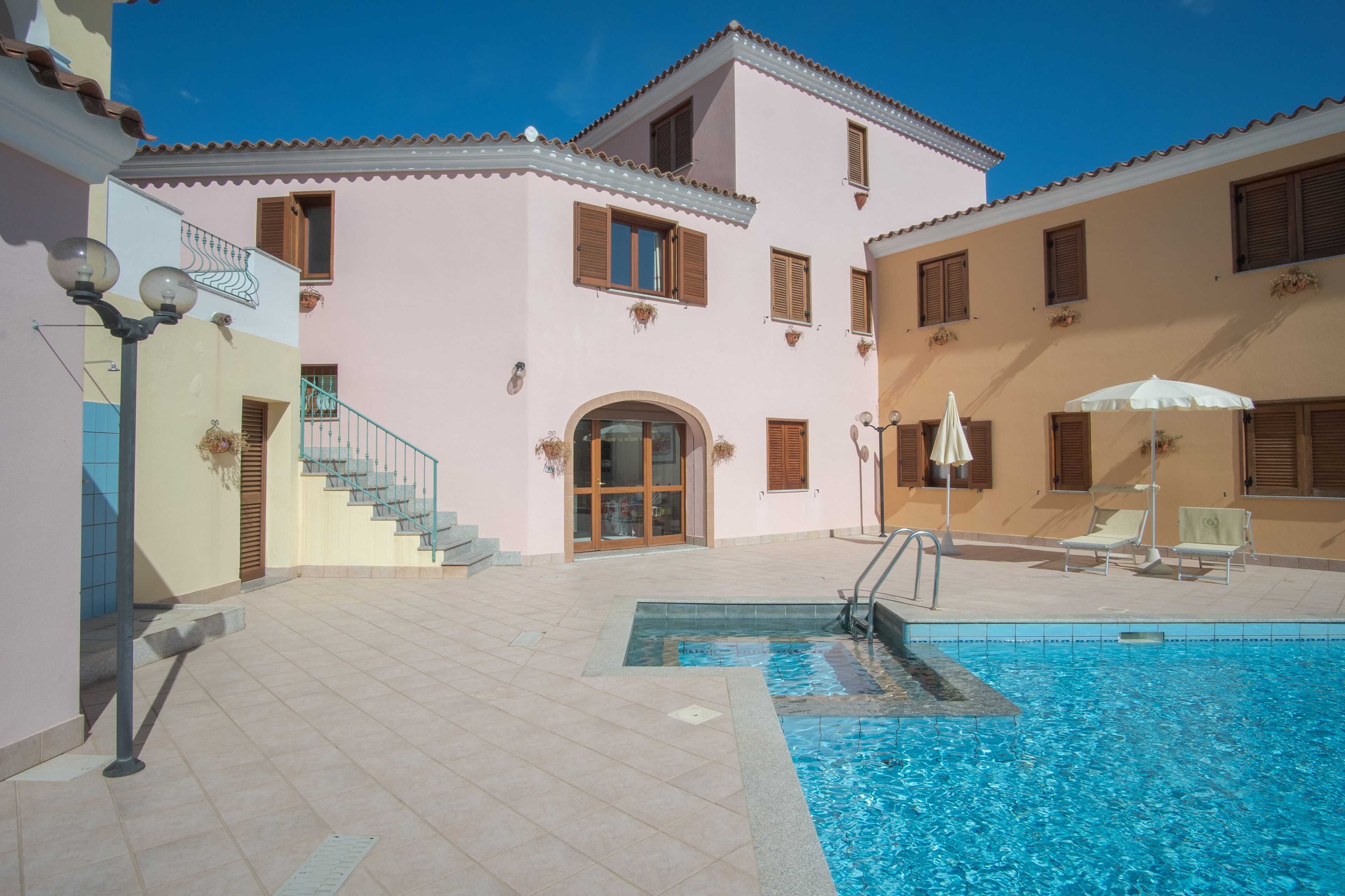 A building with a swimming pool, outdoor seating, and a staircase leading to an entrance.