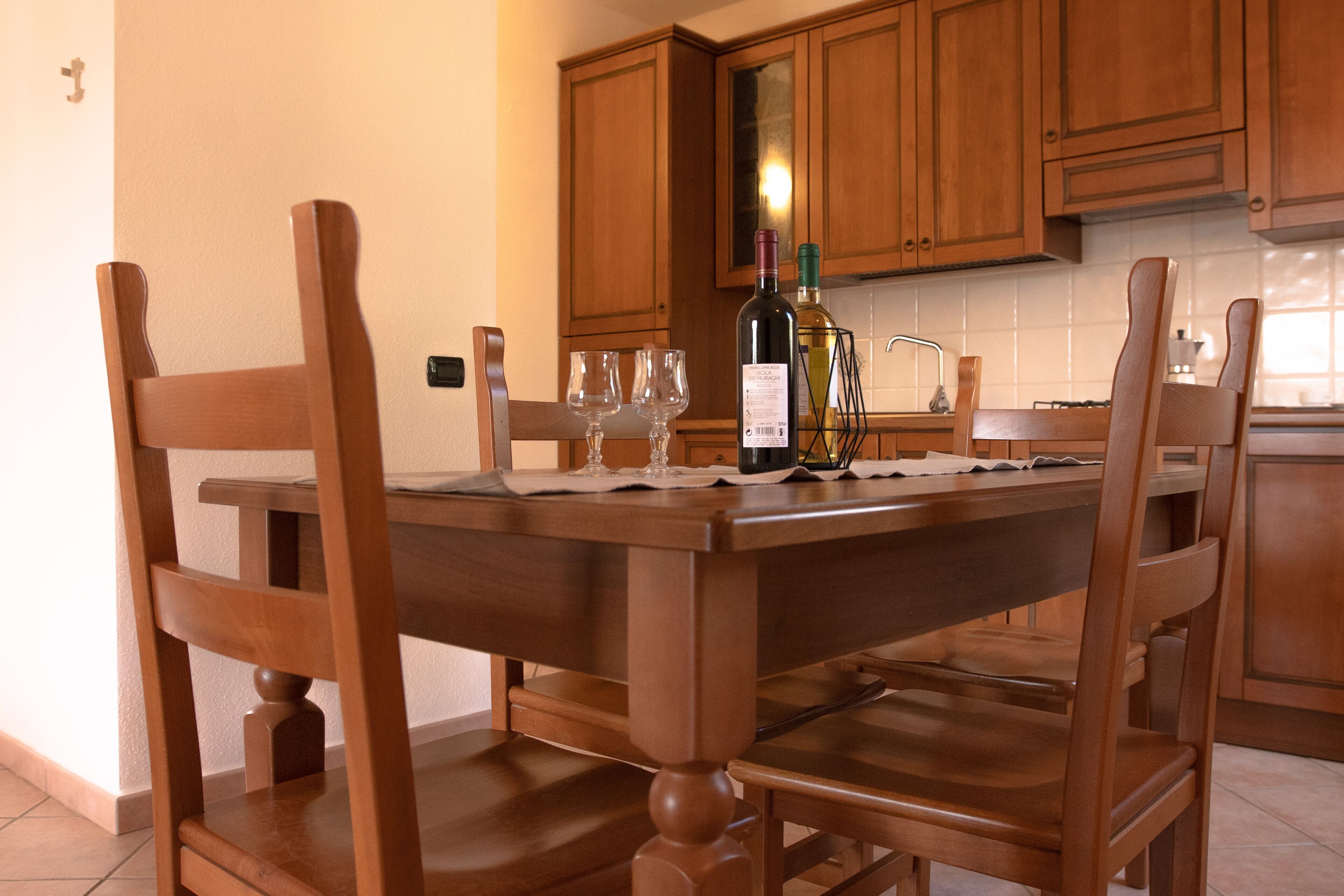 A wooden dining table with chairs, a bottle of wine, and two glasses on a placemat.