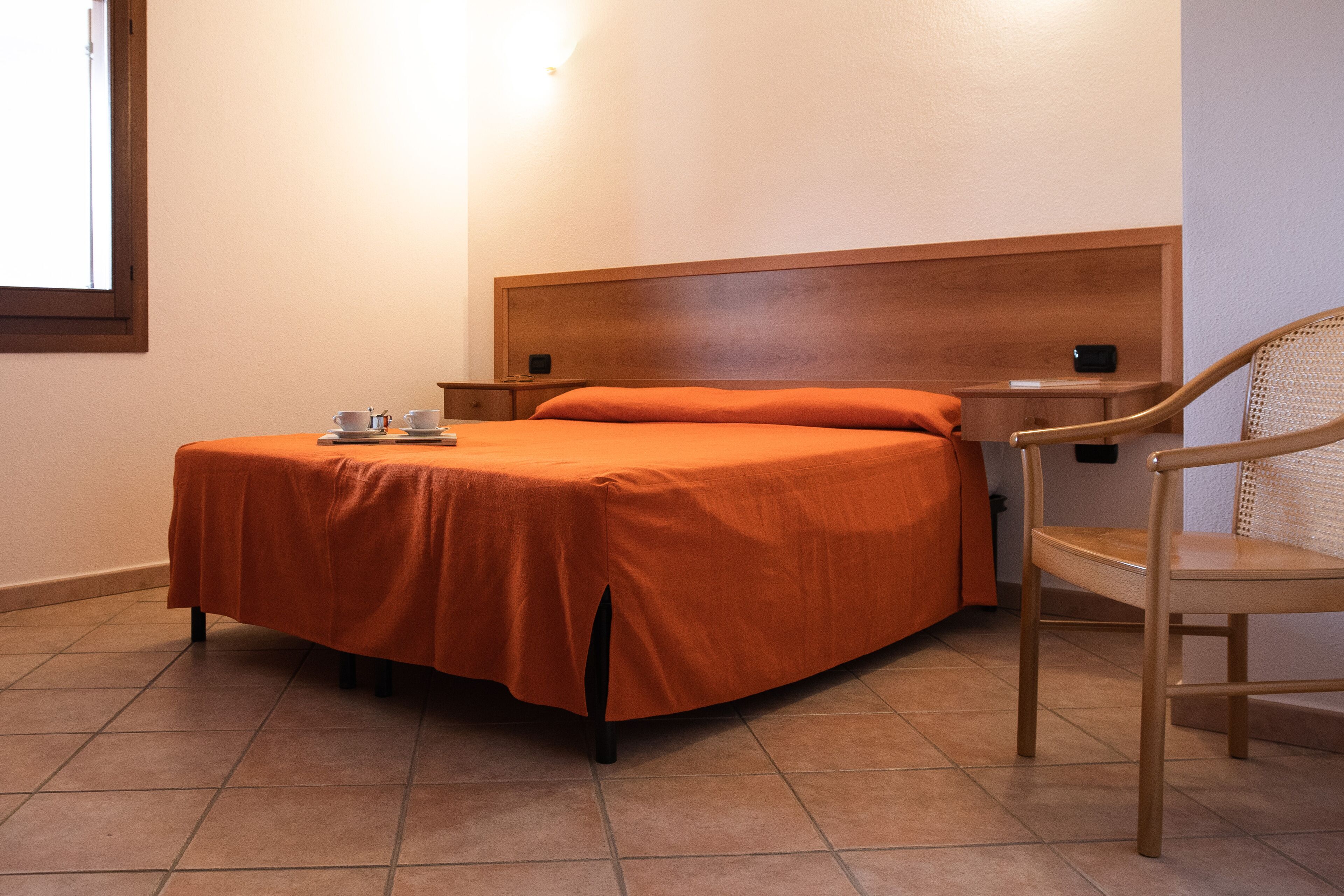 Ein Einzelbett mit orangefarbener Bettdecke, ein Holz-Kopfteil, ein Nachttisch mit Telefon und ein Stuhl.