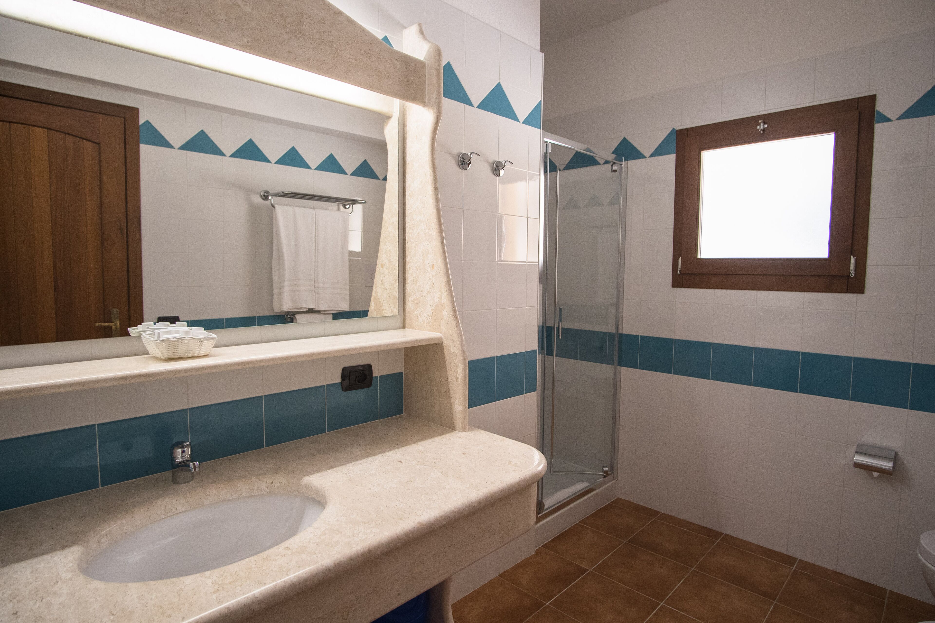 A bathroom with a glass shower, a sink, a mirror, and a window.