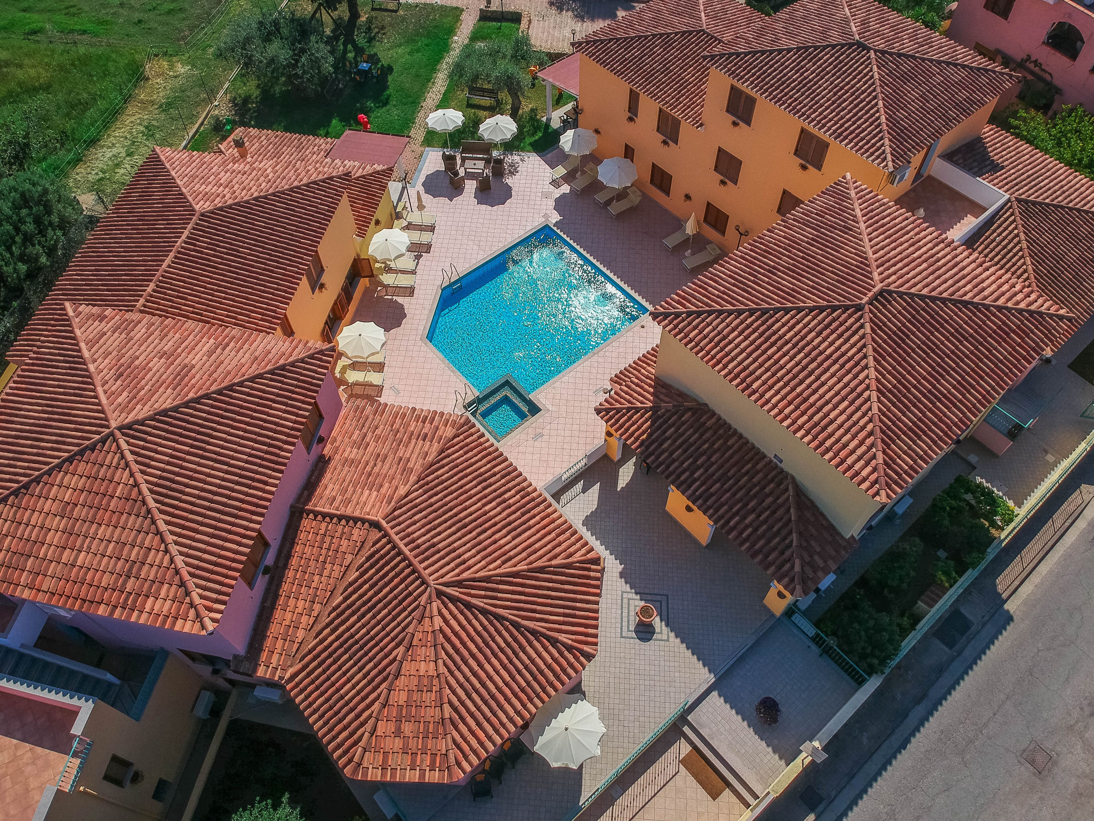 A large building with a swimming pool, outdoor seating, and a red-tiled roof.