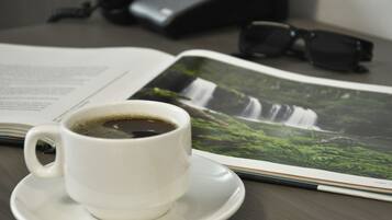 A white cup of coffee on a saucer, a pair of black sunglasses, and a magazine with a waterfall image.