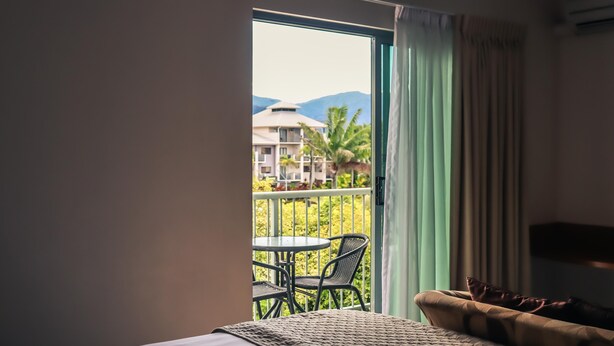 A balcony with a table and chairs, a bed with a pillow, and a view of buildings and mountains.