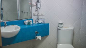 A bathroom with a sink, mirror, hairdryer, and toilet.